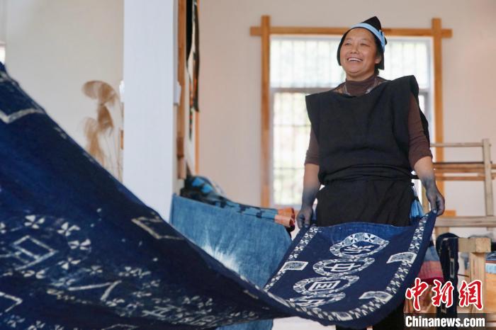 图为黎凤珍正在展示使用蓝靛染工艺制作的条幅。 韦国政 摄 图为黎凤珍正在展示使用蓝靛染工艺制作的条幅。 韦国政 摄