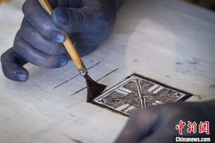 图为黎凤珍正手持着粘膏刀绘制“瑶王印”。 韦国政 摄 图为黎凤珍正手持着粘膏刀绘制“瑶王印”。 韦国政 摄