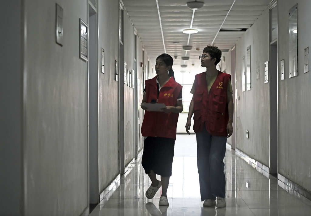 8月12日，在天津市静海区大邱庄中学集中安置点，志愿者在楼道内巡查。